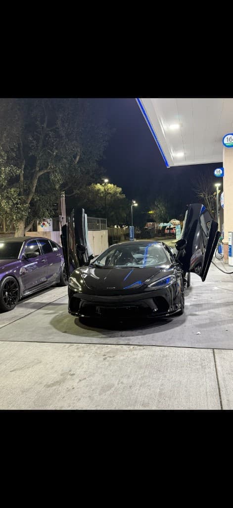 Black McLaren with dihedral doors open at a gas station